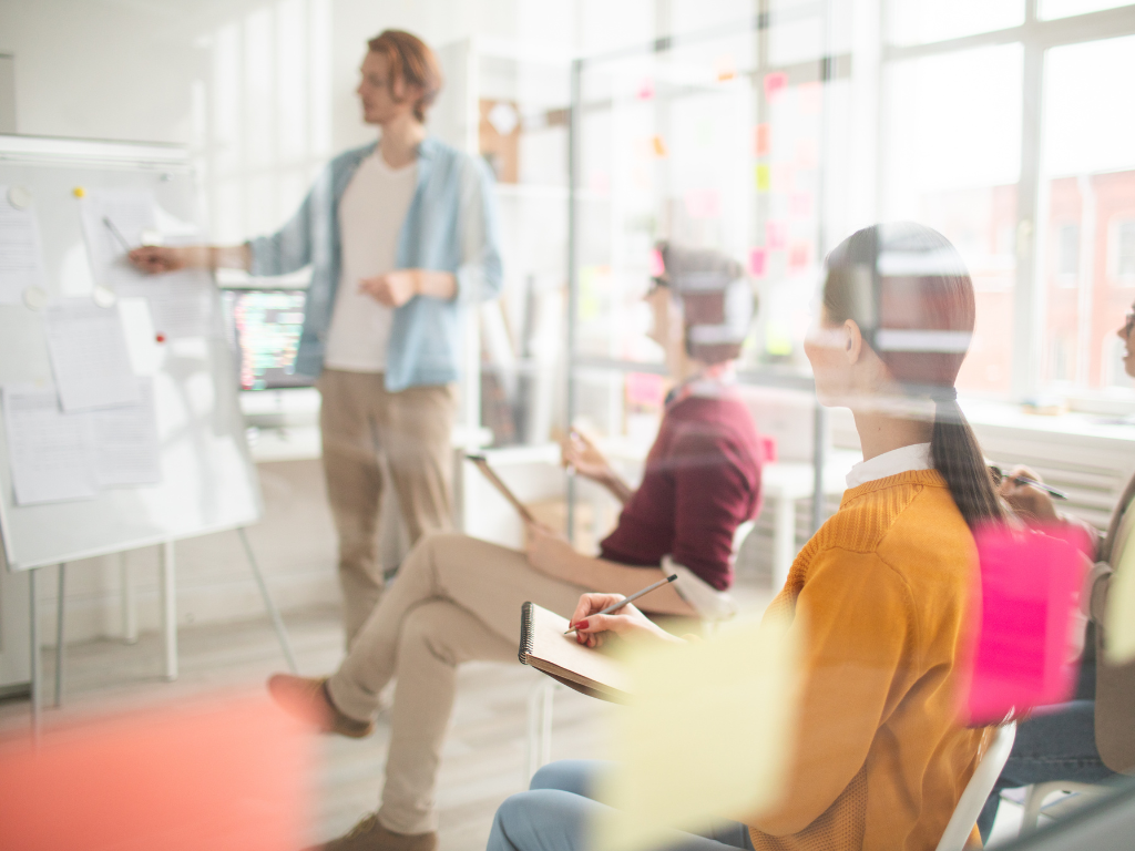 Students in classroom looking at teacher pointing at whiteboard